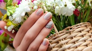 Beautiful female hand with beige nail design and flowers on background | Gorgeous Spring Nail Designs To Brighten Up The Season | Featured