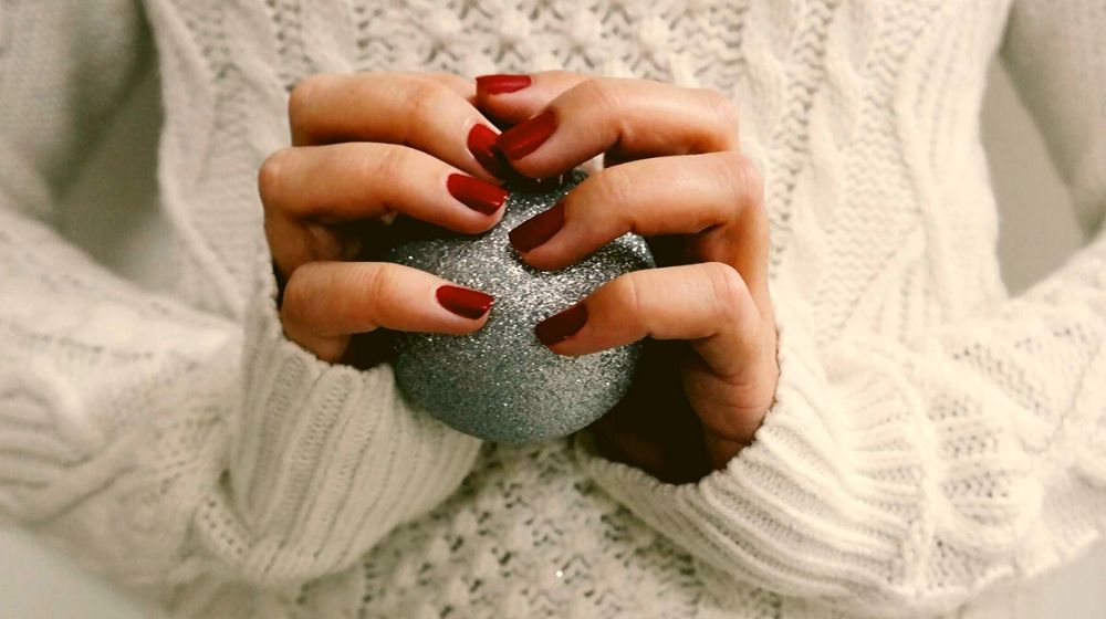 woman with red nails holding a silver Christmas ball | Sexy Red Nail Designs You Should Wear This Christmas