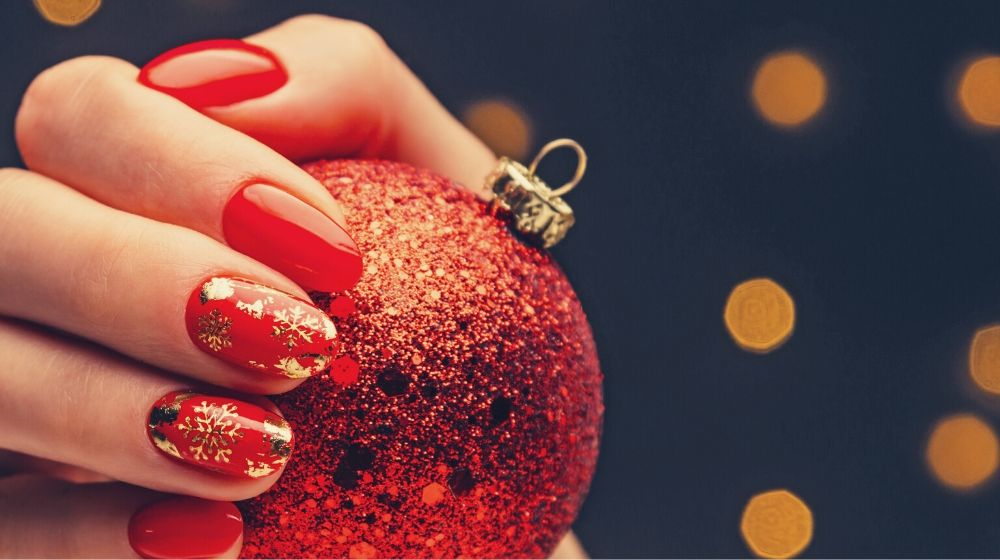 hand with red polish holding a red glittered Christmas ball | Sexy Red Nail Designs You Should Wear This Christmas
