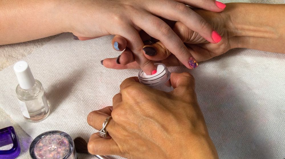 manicurist dipping fingernail into pink acrylic | Facts About Dip Powder Nails You Need Know