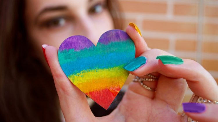 Female hand holding a rainbow colored wooden heart with her hand | Creative Rainbow Nail Designs You Must Try | rainbow nail art designs | Featured