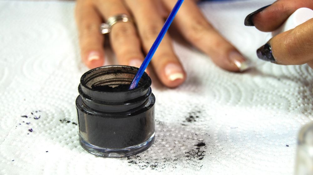 black acrylic dip powder sitting on white paper towel | Facts About Dip Powder Nails You Need Know