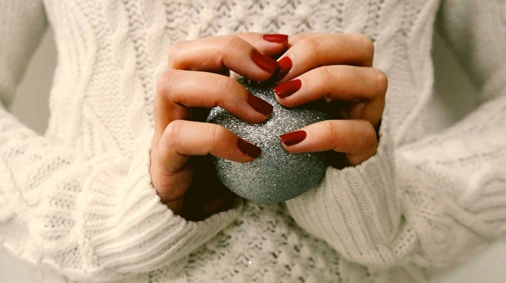 Woman holding a silver glittering Christmas ball closeup of hands and red nails | Shellac Nail Designs | Everything You Need To Know