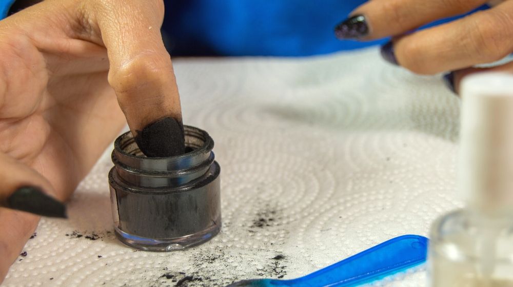 woman dipping her left thumb black | Facts About Dip Powder Nails You Need Know