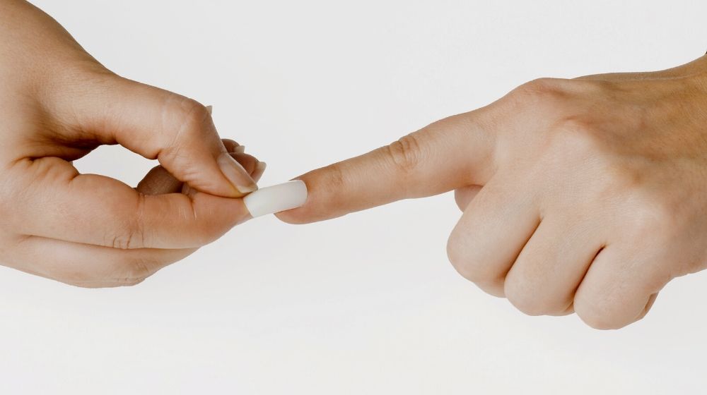 woman putting artificial fingernail on finger | Nail Biting | Everything You Need To Know